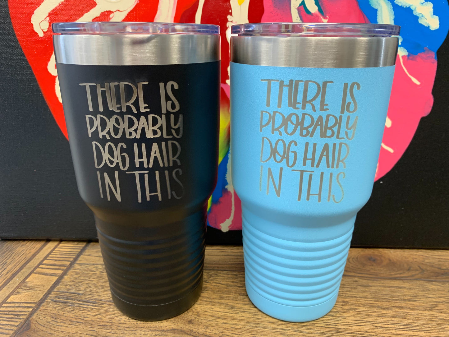 Image of two travel mugs, one in black and one in light blue, both with metal rims at the top, clear plastic lids, and the words "There is probably dog hair in this" laser etched on the side.